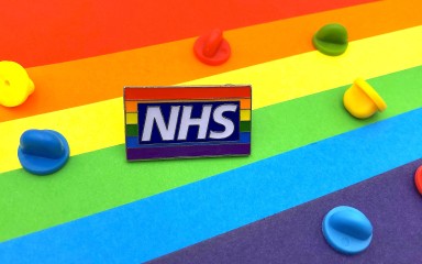 An NHS pride flag pin badges sat on a multicoloured background with rubber clutches of al the colours of the rainbow.