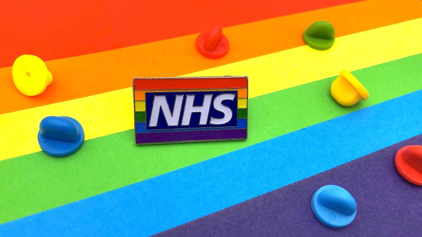 An NHS pride flag pin badges sat on a multicoloured background with rubber clutches of al the colours of the rainbow.