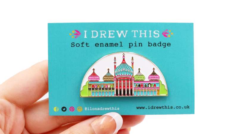 Soft enamel pin badge of a fancy building on a blue backing card that says 