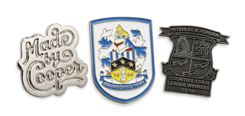 A Made by Cooper badge, Huddersfield Town pin, and a grassroots sports club badge.