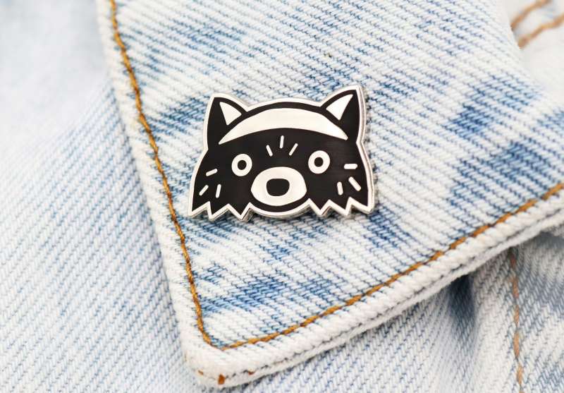 Racoon enamel pin badge on a light blue denim jacket.