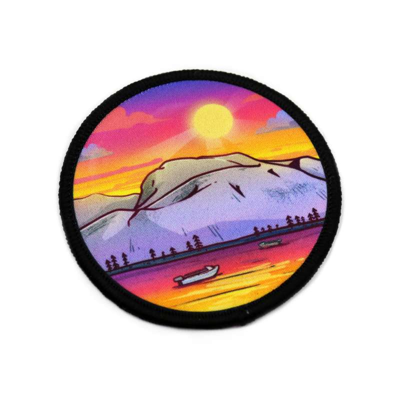 A striking woven patch depicts a sunset over a lake and mountain range scenery. A small boat floats on the water while the sun sets in a purple and pink sky.