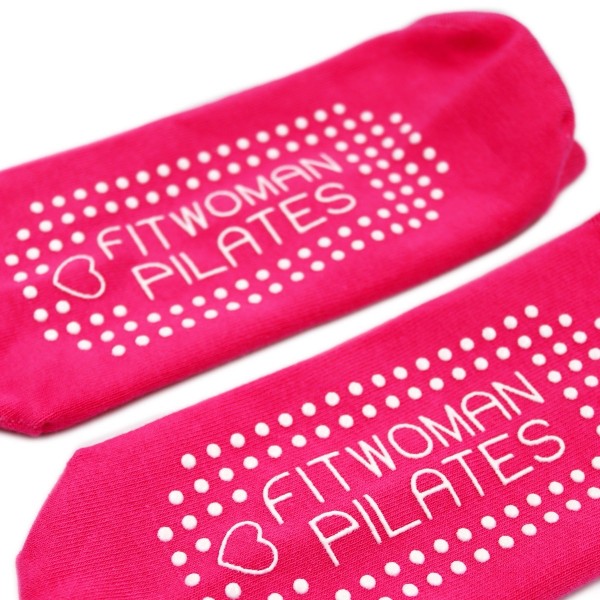 Some pink grip socks with white rubber grips on the bottom that read 'Fitwoman Pilates'.