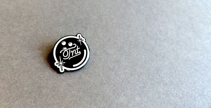 A black bowling ball pin badges with TNT written on it in a fancy font.