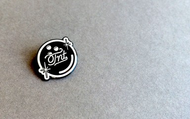 A black bowling ball pin badges with TNT written on it in a fancy font.