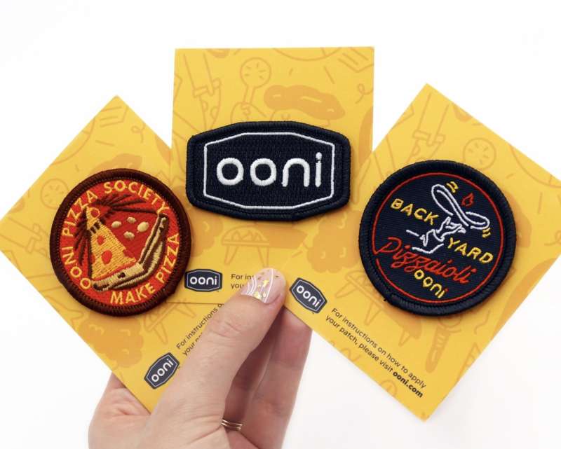 Three Ooni patches featuring the Ooni logo, a pizza society logo and the backyard pizza club emblem.