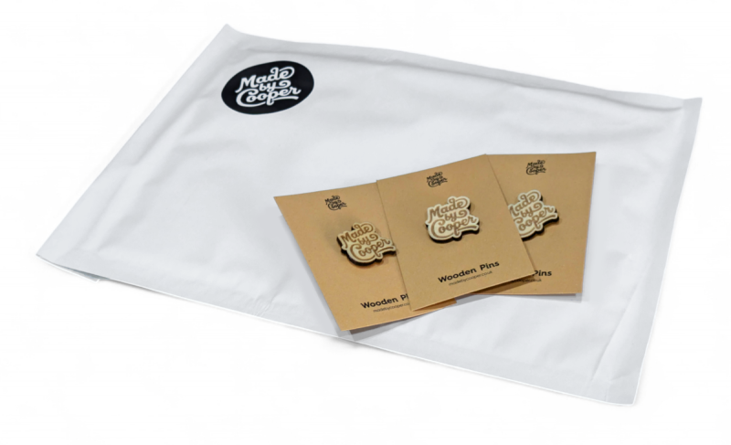 A Made by Cooper branded bubble mailer with three wooden pins with backing cards sitting on top.