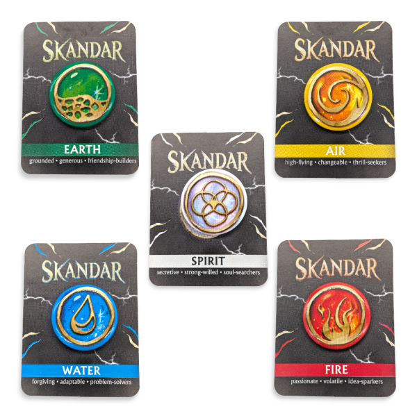 A selection of Skandar custom button badges on backing cards. These badges have patterns that represent Earth, Air, Water, Fire, and Spirit and are brightly coloured in green, yellow, silver, blue, and scarlet red.