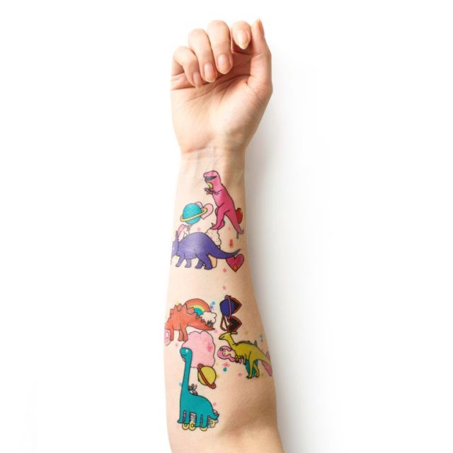 An arm featuring a vast array of colourful temporary tattoos. Featuring fake tattoos of cartoon dinosaurs.