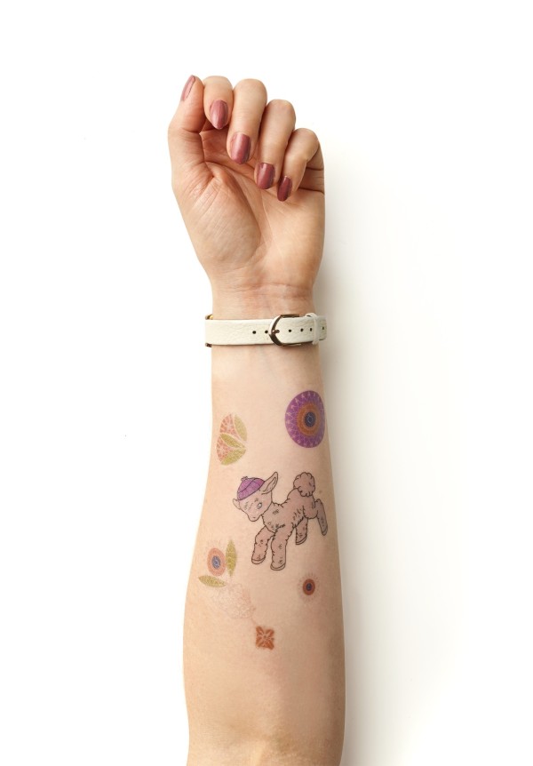 A forearm full of fun, colourful temporary tattoos featuring fake lamb tattoos wearing a wooly hat.