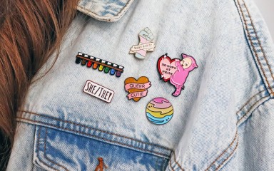 A denim jacket displaying six LGBTQ+ pin badges.