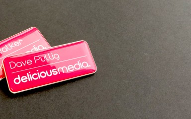 Two name badges sit on a grey carpet. The badges are red with the company name 