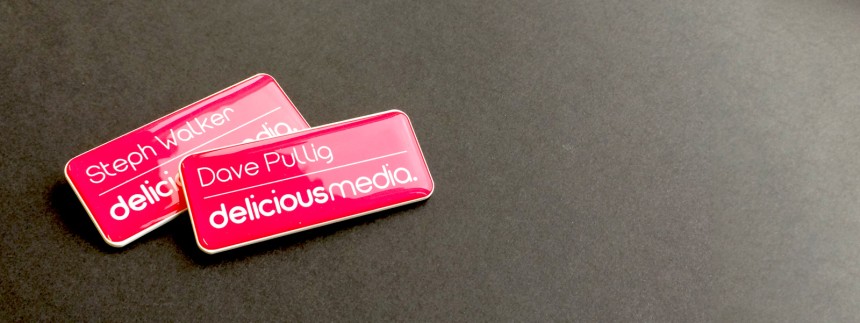 Two name badges sit on a grey carpet. The badges are red with the company name 