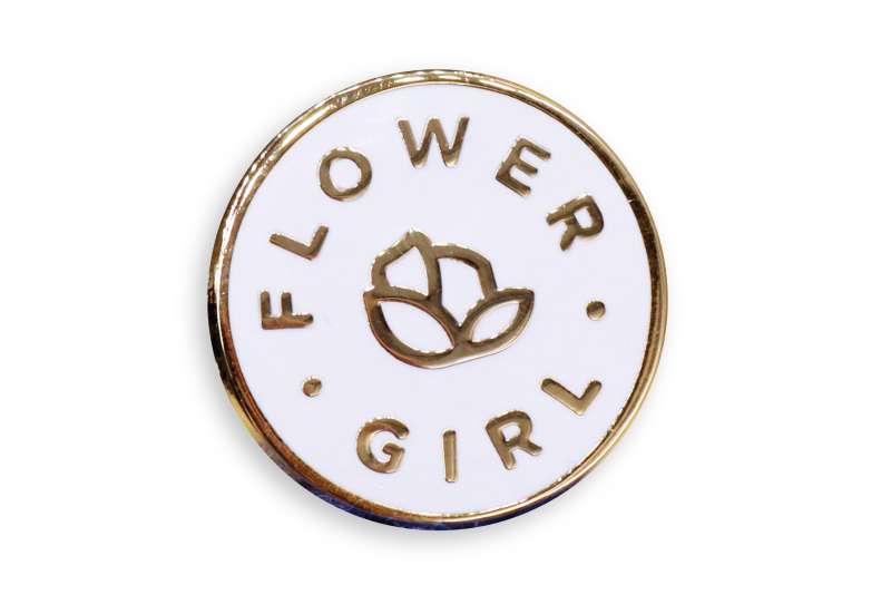 A pin badge for a flower girl in a wedding party. The pin has gold plating, a white hard enamel background and a simple flower icon in the middle.