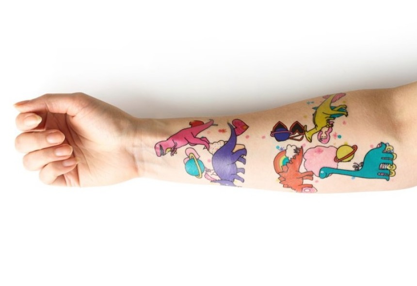 An arm the has multiple temporary tattoos applied to it featuring brightly coloured cartoon dinosaurs. 