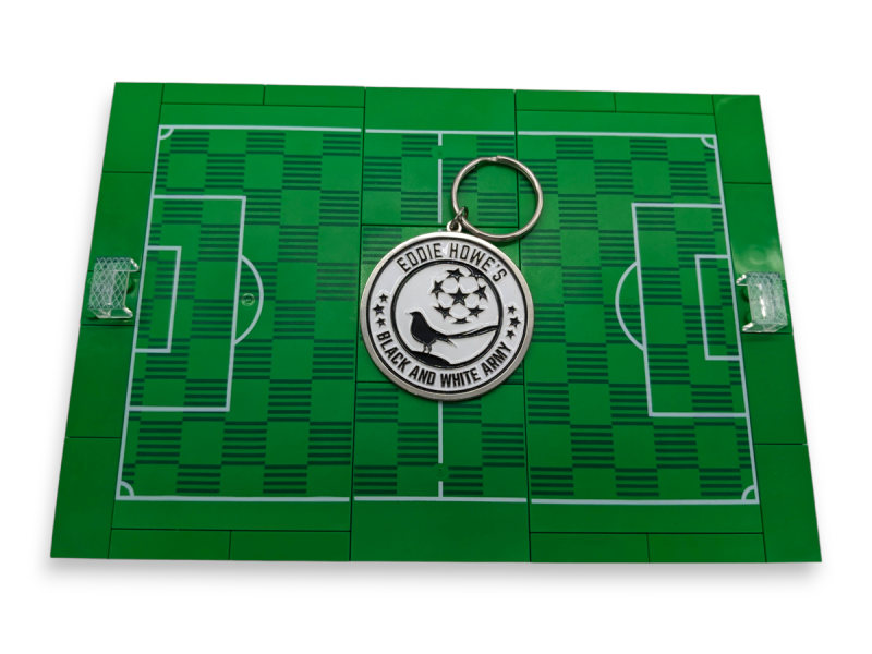 A Newcastle United keyring laid on a LEGO football pitch.