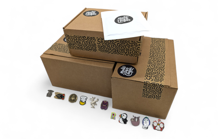 A pile of Made by Cooper branded boxes and envelopes surrounded by pin badges to show people how and why packaging for pin badges is essential.