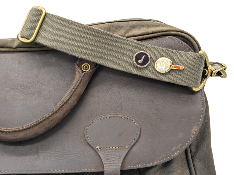 A beautiful leather satchel from Barbour with two Sherlock Holmes themed pin badges attached to the webbing strap.