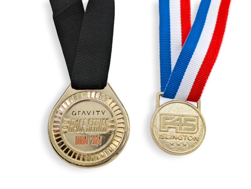 Two gold-plated medals. One for gravity series races with a black ribbon and the other that says F45 Islington with a blue, white, and red ribbon.