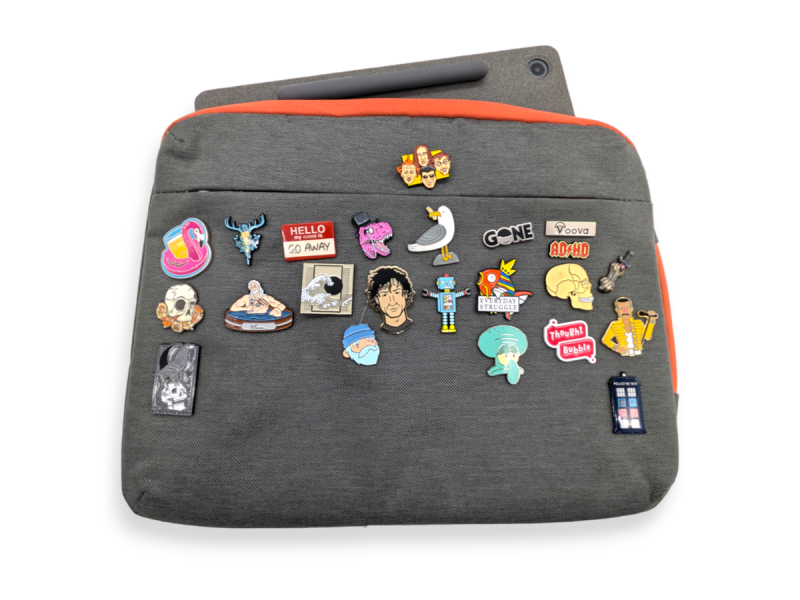 A grey laptop sleeve with orange trim covered in fun enamel pin badges.