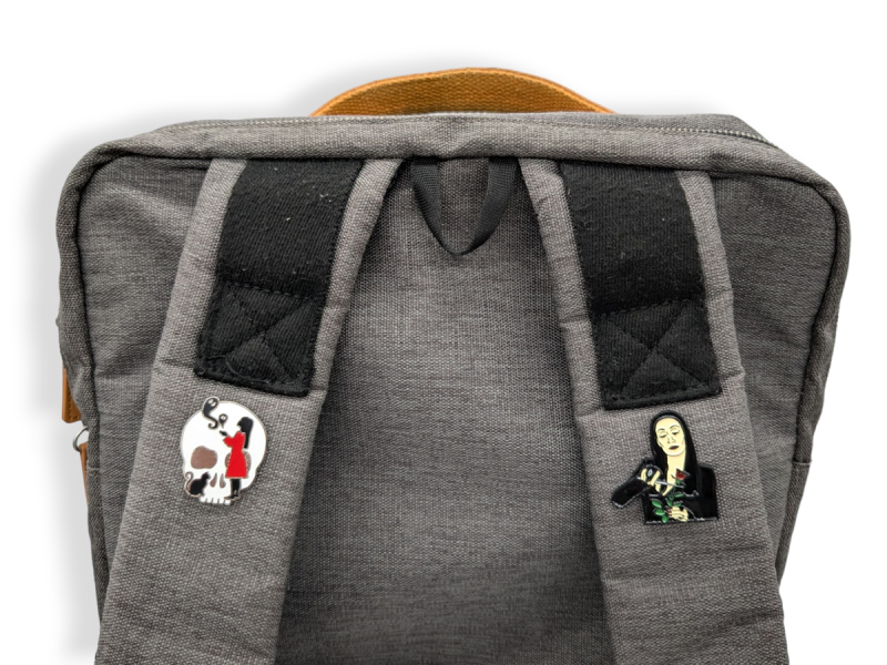 Two halloween-themed pin badges pinned on to the straps of a grey laptop backpack.