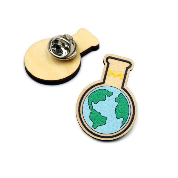 An eco-friendly wooden pin badge that features the world inside a test tube laid on its side. There's a second sustainable wooden pin badge laid on it's front so you can see the back.