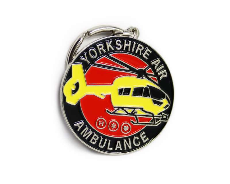 A soft enamel circular keyring featuring the yellow helicopter of the Yorkshire air ambulance on a red and black background. The words Yorkshire Air Ambulance encircle the keychain.